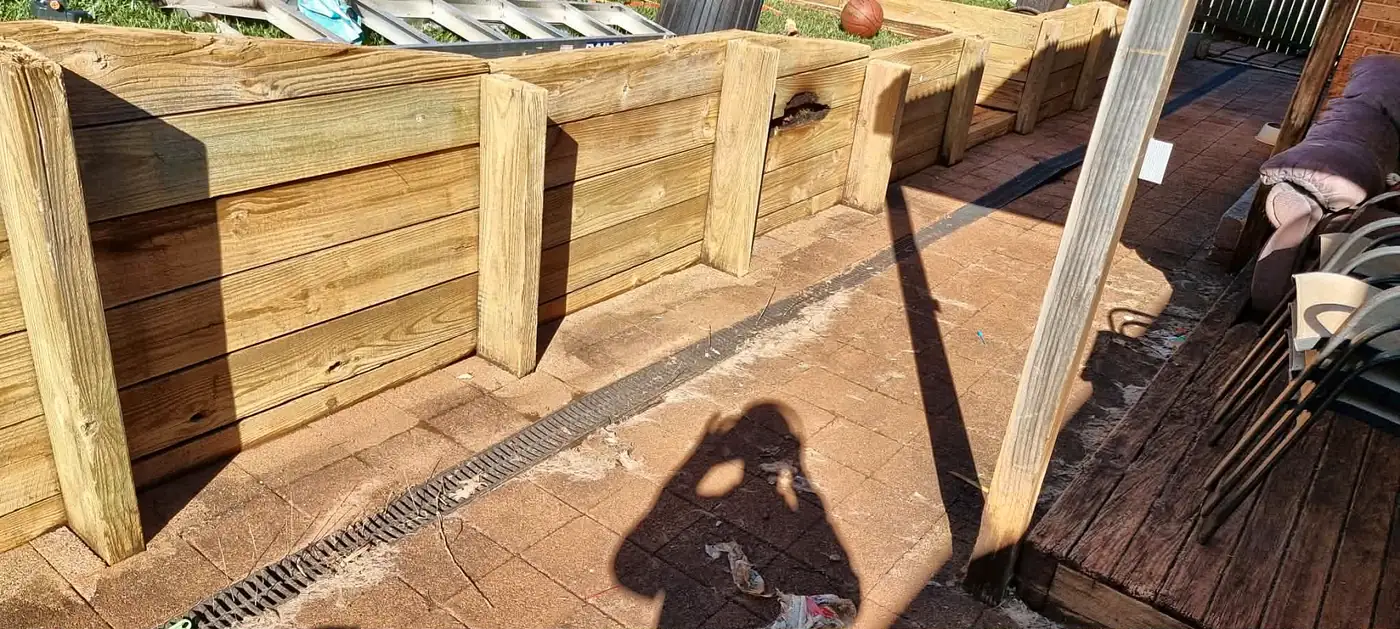 Freshly cleaned timber retaining wall above a paved courtyard