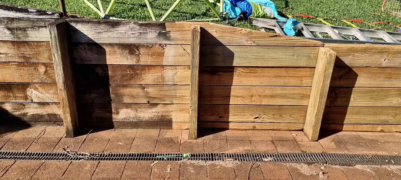 Timber retaining wall halfway through a clean, showing grey and fresh timber side by side